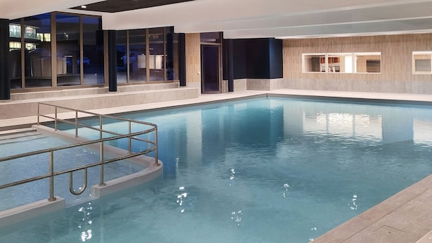 An indoor swimming pool with clear water, a metal safety railing, and a modern interior design with large windows and wooden accents. - Résidence Odalys Collection L'Eclose by Interhome (L'Alpe d'Huez)