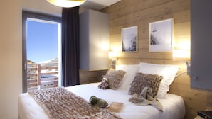 A hotel room with a large bed, wooden headboard, two framed pictures, a bedside lamp, and a view of the outside. - Résidence Odalys Collection L'Eclose by Interhome (L'Alpe d'Huez)