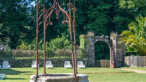 A garden with a stone fountain, white chairs, and an archway. - Odalys Référence Le Château de Kéravéon by Interhome (Erdeven)