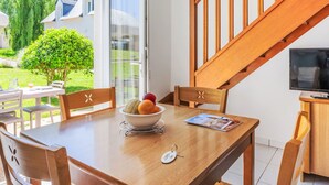 A dining area with a wooden table, chairs, and a bowl of fruit. A staircase with wooden railings is visible in the background. - Rés. Odalys Référence Horizon Morgat by Interhome (Crozon-Morgat)