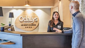 Un mostrador de recepción con un letrero de madera que dice 'Odalys Vacances Le Mont d'Auron' y una tarjeta de identificación para un miembro del personal.