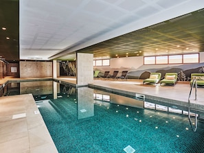 Una piscina interior con suelo de baldosas, sillones de descanso y un mural en la pared.