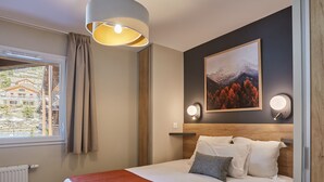 Habitación de hotel con una cama, una ventana que ofrece vistas a edificios, un cuadro en la pared y dos luces fijadas a la pared.