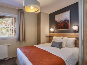 Habitación de hotel con una cama, una ventana que ofrece vistas a edificios, un cuadro en la pared y dos luces fijadas a la pared.