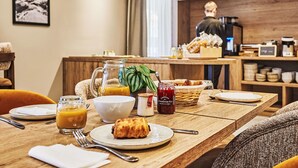 Une table mise pour le petit-déjeuner, avec une place pour deux personnes, comprenant un croissant, un verre de jus d’orange, un bol et un pot de confiture.