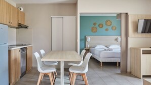 Eine moderne Küche mit Esstisch und Stühlen, ein Bett mit Kopfteil sowie ein an der Wand befestigter Fernseher.