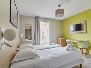 Ein Hotelzimmer mit zwei Betten, einem Schreibtisch, einem Stuhl, einem Fernseher und einem Balkon mit Aussicht.
