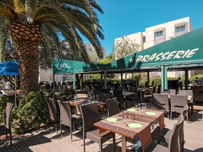 An outdoor dining area with wicker furniture and a green awning labeled "BASSERIE". - Odalys Référence Les Océanides by Interhome (La Londe Les Maures)