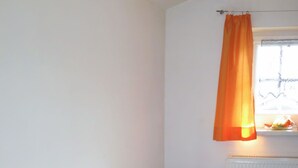 A small room with a table and chairs, a window with an orange curtain, and a radiator.