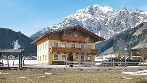 A two-story building with a balcony, surrounded by snow-covered mountains and a clear sky.