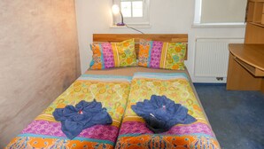 A small, cozy bedroom with a single bed, colorful bedding, a wooden headboard, a window with a view, and a radiator.