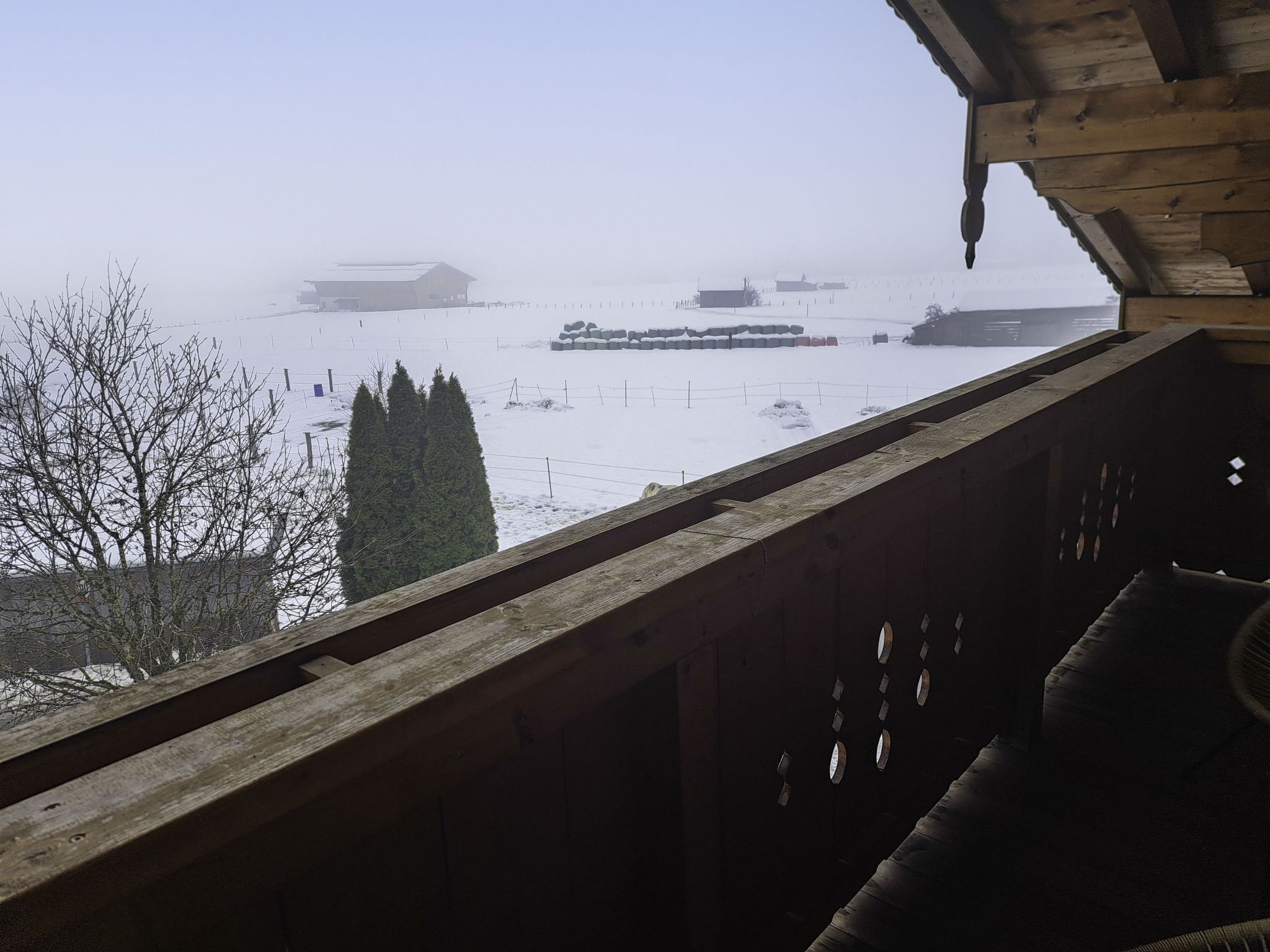 A snowy landscape with a wooden balcony overlooking a farm.