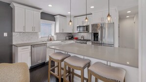 A modern kitchen with white cabinets, stainless steel appliances, and a large island with bar stools. - Cozy, Beautiful Birmingham 4BR/2BA Getaway! (Birmingham)
