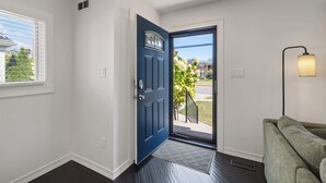 A clean, modern entryway with a dark blue door, a white wall, a green couch, and a floor lamp. - Cozy, Beautiful Birmingham 4BR/2BA Getaway! (Birmingham)