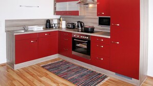 Una cocina compacta con armarios rojos, horno integrado y microondas.