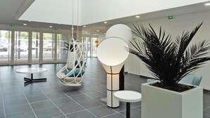 Eine moderne Lobby mit hoher Decke, einem Hängekorbstuhl, einer großen Topfpflanze und einer Sitzecke mit Tisch.