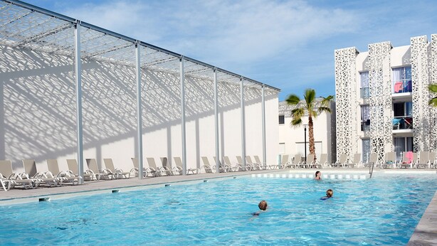 Ein Schwimmbecken mit Liegestühlen und ein Gebäude mit einer verzierten Fassade.