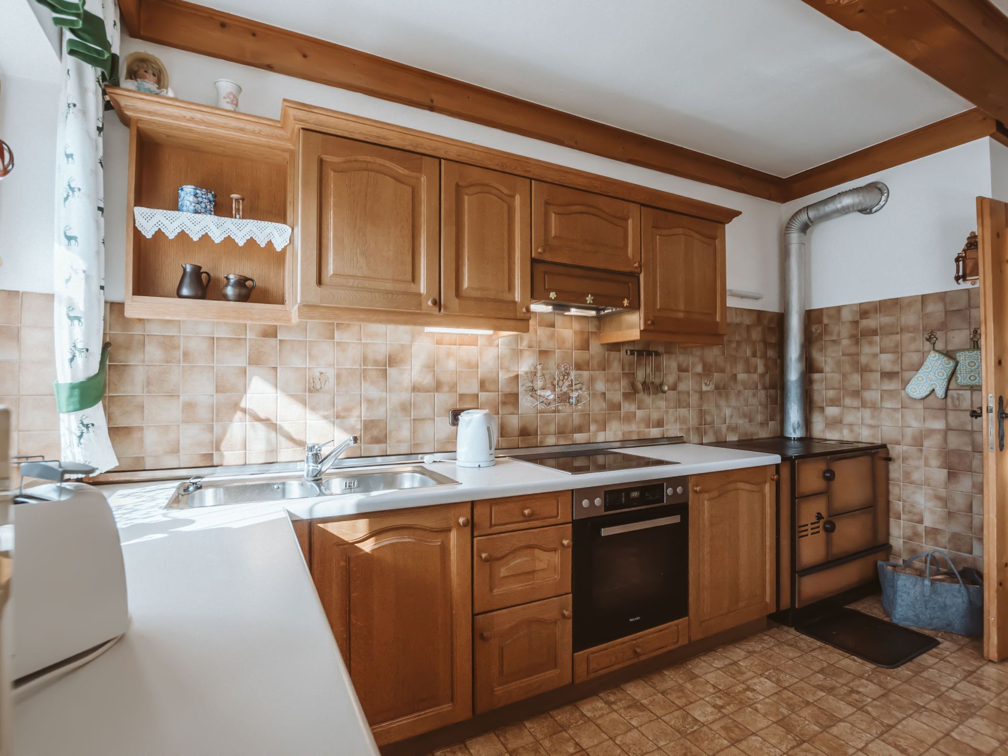 Een keuken met houten kastjes, een wit aanrecht, een fornuis en een spoelbak.