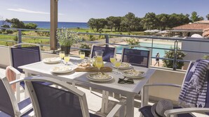 A balcony with a table set for breakfast, overlooking a pool and the sea. - Résidence Odalys Référence Acqua Bella by Interhome (Moriani-Plage)