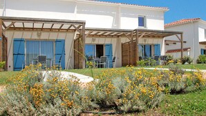 A two-story building with a covered patio area, outdoor seating, and a garden with yellow flowers. - Résidence Odalys Référence Acqua Bella by Interhome (Moriani-Plage)
