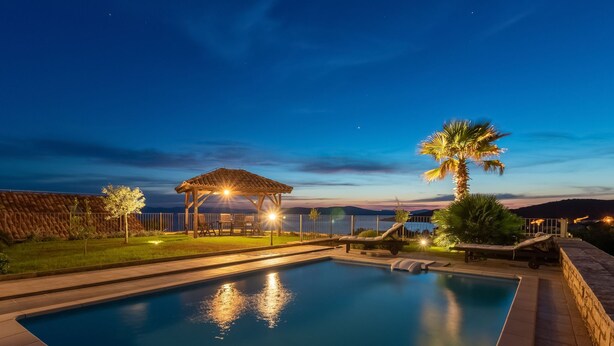 A swimming pool with a gazebo and lounge chairs, surrounded by a landscaped garden and a view of the sea at dusk. - Villa Bugenvila by Interhome (Ugljan/Ugljan)