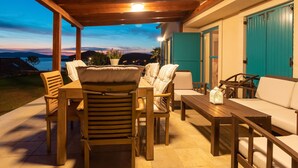 An outdoor patio with wooden furniture, a view of the sea, and teal doors. - Villa Bugenvila by Interhome (Ugljan/Ugljan)