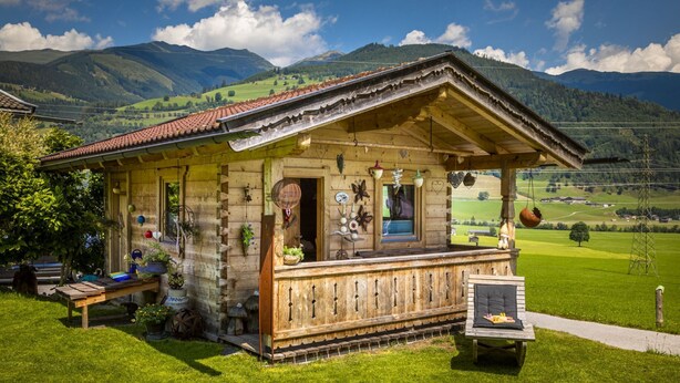 Un chalet en bois doté d’un balcon, entouré de prairies verdoyantes et de montagnes.