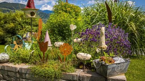 Un jardin agrémenté de diverses sculptures et plantes, un mur de pierre et un ciel dégagé.