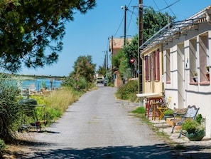 Eine schmale Straße führt zu einem Gebäude mit Balkon, umgeben von viel Grün und blauem Himmel.