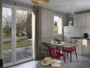 Eine moderne Küche mit Essbereich, Glastüren zu einer Terrasse und Blick auf Bäume und eine Straße.