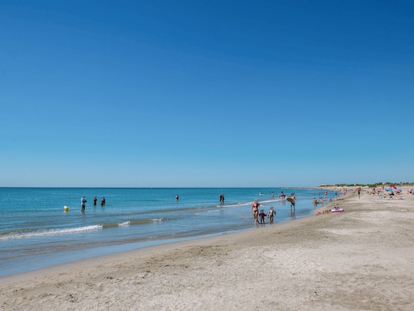Ein Strand mit Menschen, die am Ufer entlanggehen, einige im Wasser, und Strandbesucher, die in der Sonne entspannen.