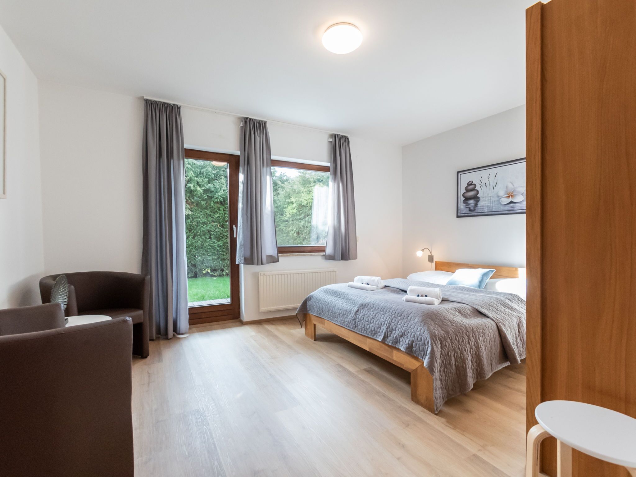 A bedroom with a bed, a chair, a table, and a window with curtains.