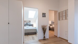 A hallway leading to a bedroom with a skylight, a bedside table with a vase, and a framed picture on the wall. - Alpenchalets by Interhome (Zell am See)
