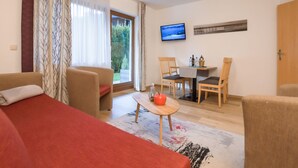 A room with a bed, a sofa, a dining table with chairs, a TV, and a window with curtains. - Alpenchalet by Interhome (Zell am See)