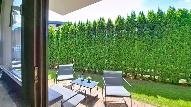 An outdoor patio with two chairs and a table, a wooden deck, and a hedge in the background. - Alpenchalet by Interhome (Zell am See)