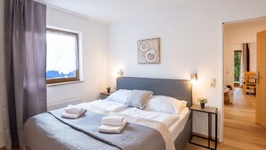A modern bedroom with a large bed, bedside tables, a window with curtains, and a view of the outdoors. - Alpenchalet by Interhome (Zell am See)