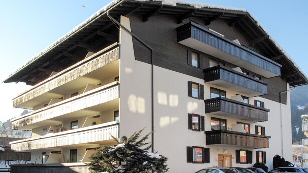 A multi-story building with balconies, a snow-covered ground, and parked cars. - Apartment Leif by Interhome (Zell am See)