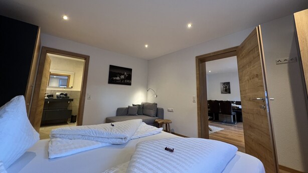 A hotel room with a bed, a desk, a chair, a mirror, and a door leading to a dining area. - Stefanie by Interhome (Bruck)