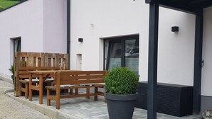 A wooden bench and table set up outside a building with a white exterior and a black door. - Stefanie by Interhome (Bruck)