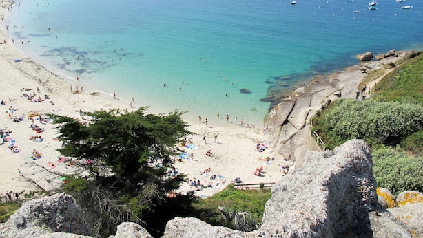 Een strand met helder turquoise water, rotsformaties en boten.