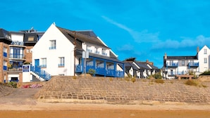 Een gebouw aan de kust met een stenen muur en een strand op de voorgrond.