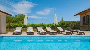 A pool area with lounge chairs and umbrellas, surrounded by greenery and a clear sky. - Vacation home Ana by Interhome (Labin)