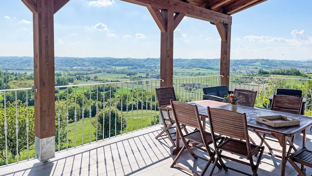 Ein überdachter Außenbereich mit Holztisch und Stühlen, der einen Blick auf eine grüne Landschaft bietet.
