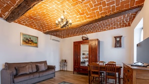 Ein gemütliches Wohnzimmer mit Ziegeldecke, einem Holzesstisch mit Stühlen, einer Couch, einem Fernseher und einer Holzkommode.