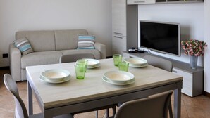 A modern living room with a sofa, a dining table with plates and glasses, a flat-screen TV, and a small shelf with decorative items. - La Casara B by Interhome (Lazise)