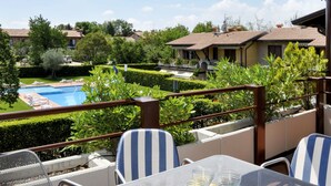 A poolside area with a view of a swimming pool, neatly trimmed hedges, and a row of houses in the background. - La Casara B by Interhome (Lazise)