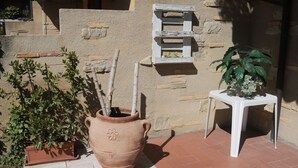 Una maceta de terracota con una planta, una mesa pequeña blanca con una planta, y un jarrón de pared con una planta.