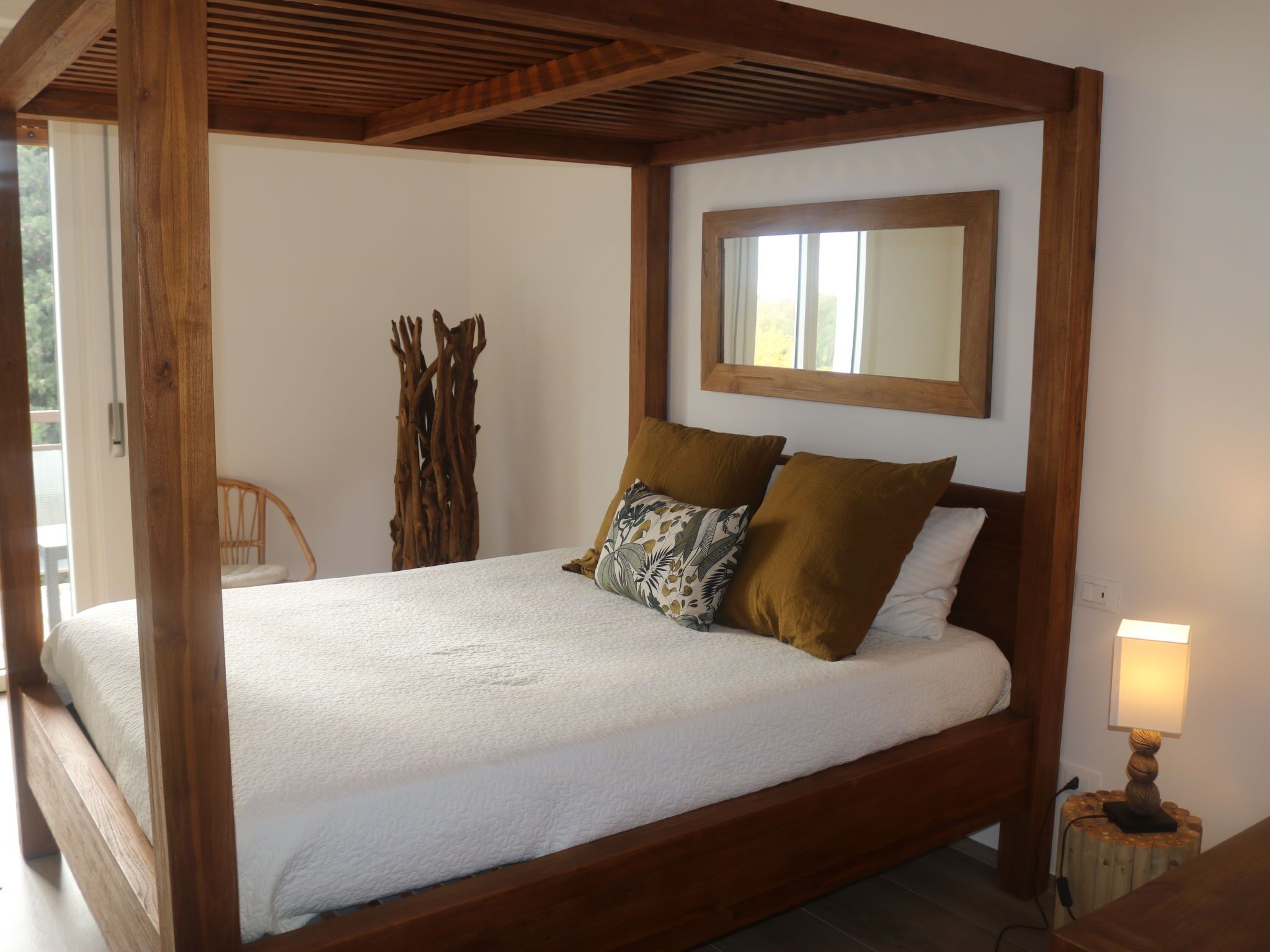 Uma cama com estrutura de madeira, roupa de cama branca, cabeceira de madeira e uma luminária de cabeceira.