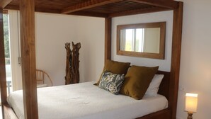 Uma cama com estrutura de madeira, roupa de cama branca, cabeceira de madeira e uma luminária de cabeceira.