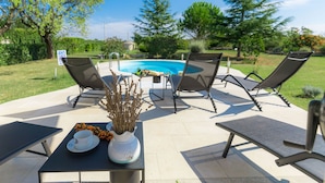 A poolside area with lounge chairs, a table with a vase of dried flowers, and a view of a swimming pool. - Vacation home Bozac by Interhome (Pula/Vodnjan)